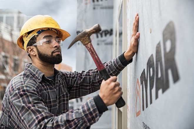 Construction worker hammers fasteners into commercial building wrap